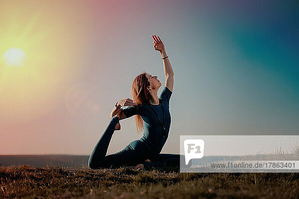 Woman in blue sports wear practicing yoga on sky background