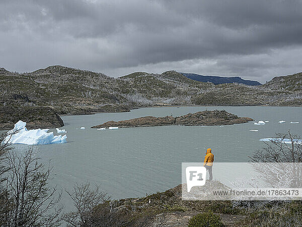 One man stands on a rock at the coast of a lake with icebergs