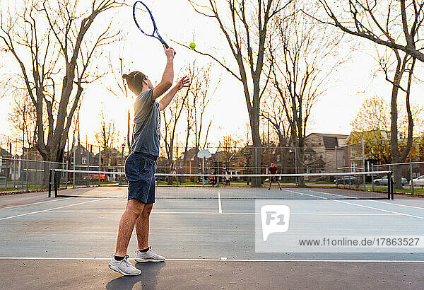 Teenage boy playing tennis on outdoor hard court in spring.