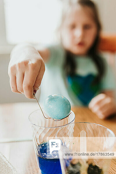 Close up of young girl dying an easter egg blue at home