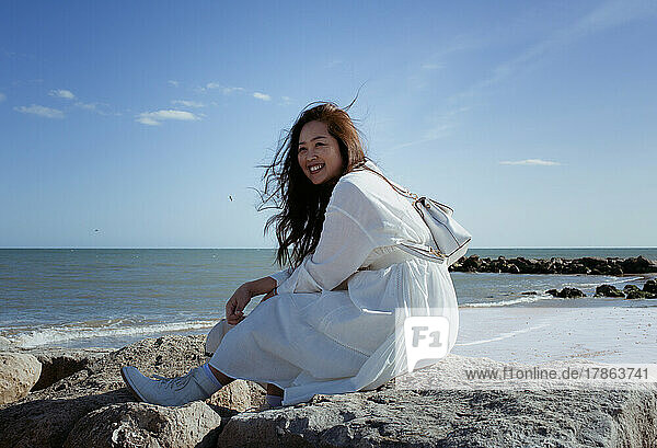 beautiful Asian woman sat on some rocks by the beach in summer