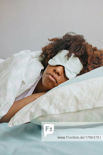 Curly African woman sleeping in apartment with sleep mask on her face.