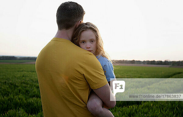 father carrying a tired daughter through a field at sunset