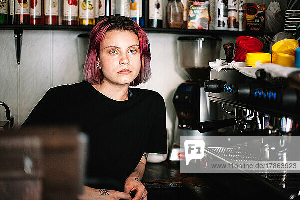 Young female barista sitting by coffee machine in coffee shop