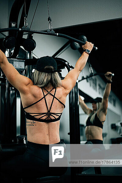 Muscular woman using machine at gym wearing black workout clothi