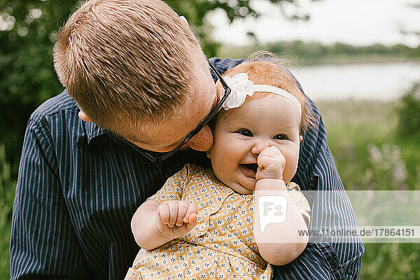 Baby daughter smiles and laughs while father holds and hugs her