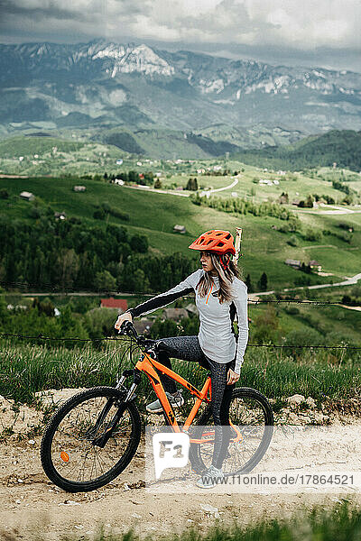 Young cyclist sitting on her bicycle against mountains