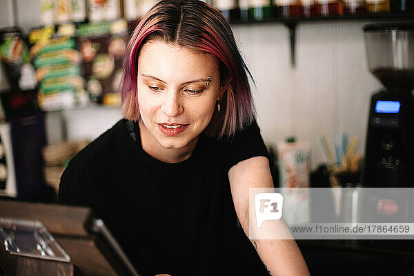 Happy young female barista working at checkout counter in coffee shop
