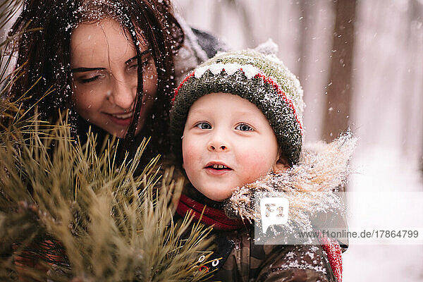 Happy mother and son standing by Christmas tree outdoors in winter