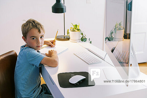 little boy doing homework in his room at his desk by the computer