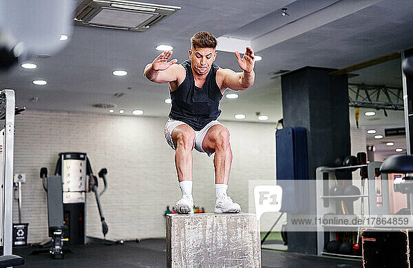 Man jumping mid air on gym box with arms reaching out