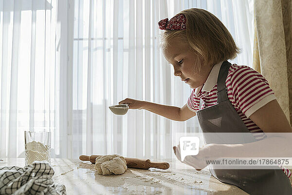 The girl in the kitchen cooks from dough and flour.