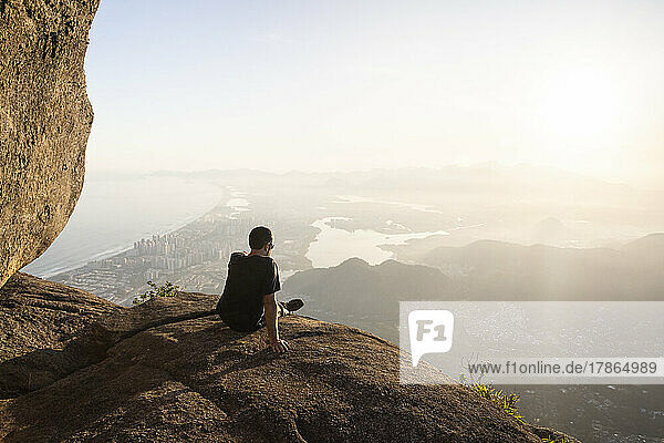 Man enjoying beautiful sunset view to city from rocky mountain top