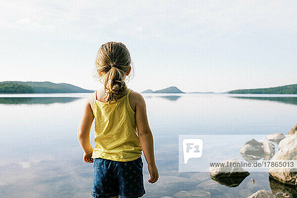 little toddler girl standing by a crystal clear lake
