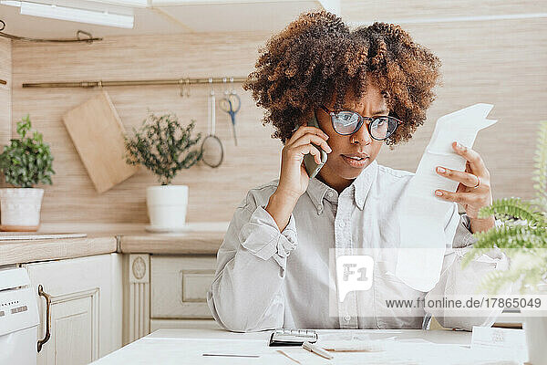 Woman talking on the phone looking bills for payment in the kitchen.