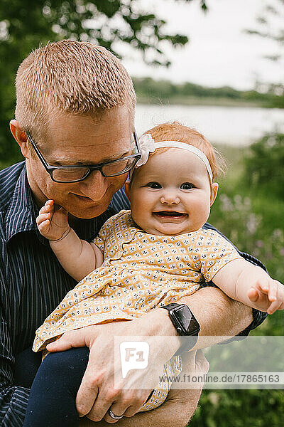 Dad holds and hugs smiling and happy baby red head daughter