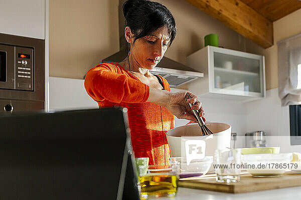 Woman in orange sweater whisking eggs on a white bowl.