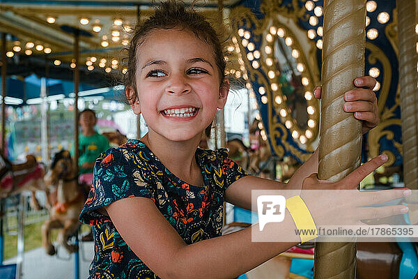Young girl riding carousel with toothy smile