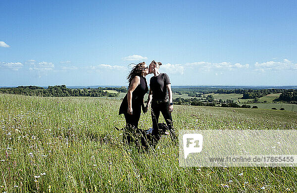 lesbian couple kissing whilst walking their dog in a beautiful meadow