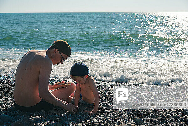 A little boy and his father sit near the sea and play.