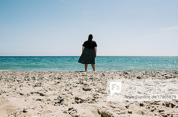woman stood alone on the sand looking at the sea on a sunny day