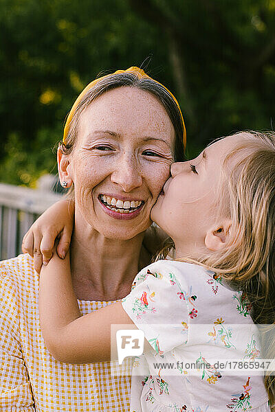 Young daughter gives smiling happy mother kiss on cheek