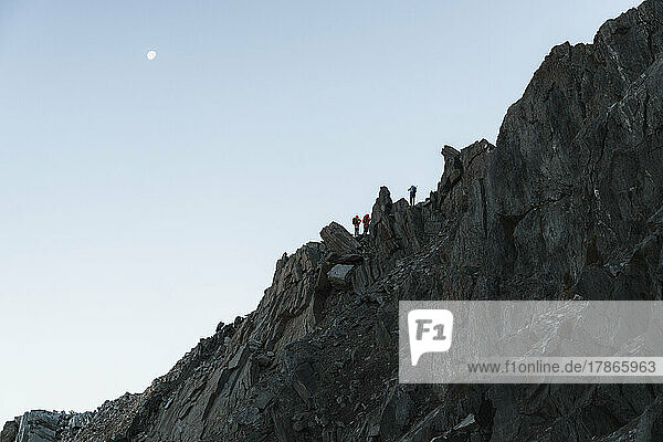 Climbers exposed on ridge line in front of moon against the sky