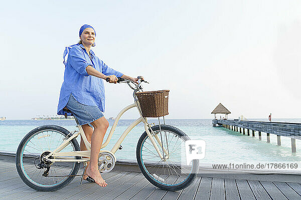 A woman on a bicycle on the ocean in the Maldives.