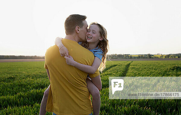 father carrying his daughter laughing whilst walking at sunset