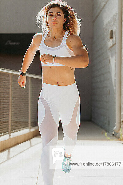 Fitness model running outdoors with sunshine wearing white worko