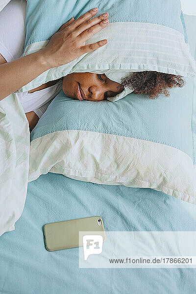 Woman sleeping with a pillow on her head and a phone nearby