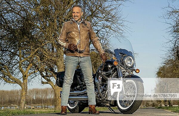 Middle-aged man with leather jacket standing in front of his motorbike and holding sunglasses  Karlsruhe  Germany  Europe