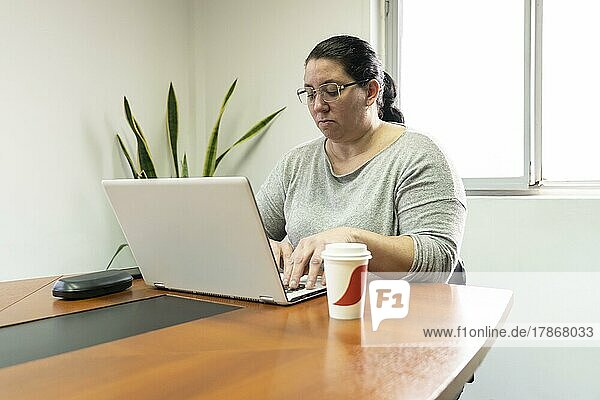 Reife Geschäftsfrau  die am Kopf des Tisches in einem Bürobesprechungsraum sitzt und an ihrem Computer arbeitet