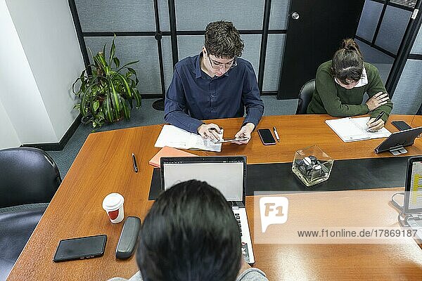 Eine Gruppe von Mitarbeitern sitzt um den Besprechungstisch im Büro und arbeitet an ihren Laptops und Notizblöcken