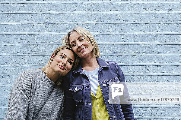 Smiling woman leaning on mother in front of blue wall