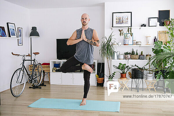 Bald man practicing tree pose in living room at home