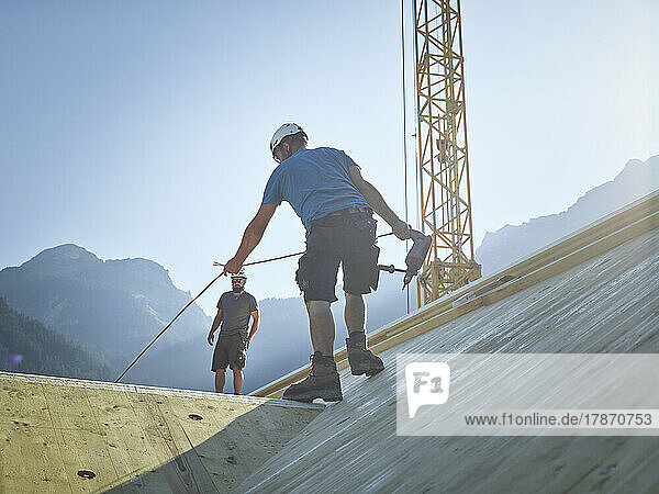 Carpenter holding drill working on roof at construction site