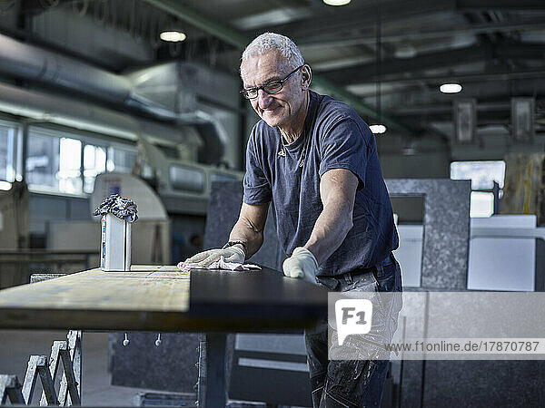 Smiling stonemason polishing stone slab at workshop
