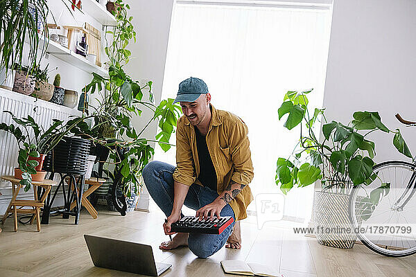 Lächelnder Mann lernt Klavier  indem er sich zu Hause ein Online-Tutorial auf dem Laptop ansieht