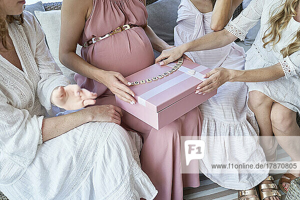 Hands of pregnant woman opening gift box sitting with friends