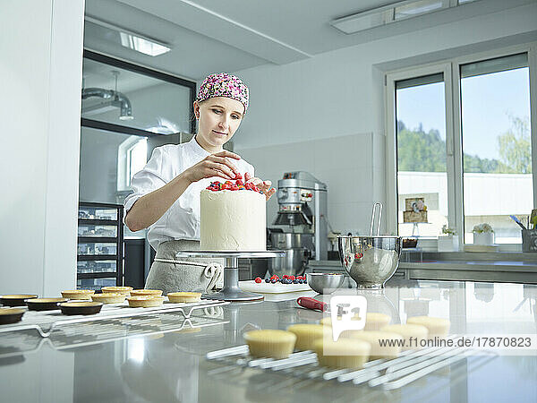 Young confectioner decorating cake with strawberries in kitchen