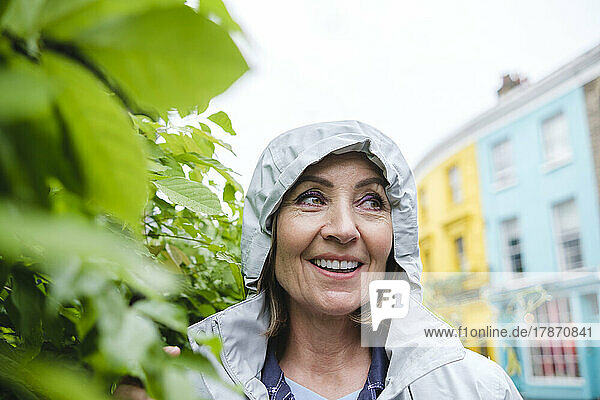 Smiling senior woman wearing windbreaker by plants