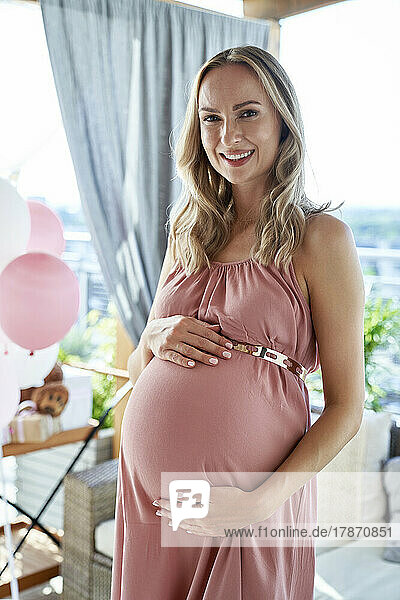 Glückliche schwangere Frau trägt rosa Kleid bei der Babyparty