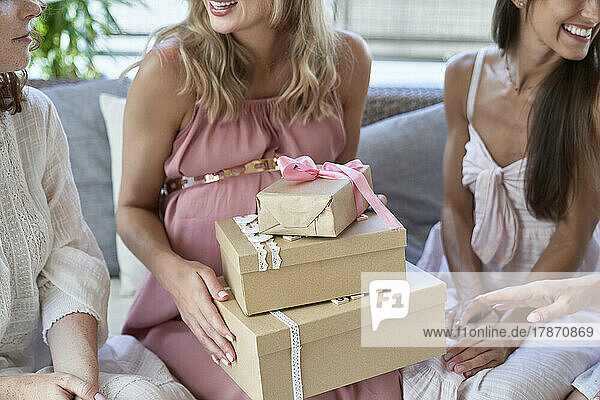 Pregnant woman holding gift boxes by friends at baby shower