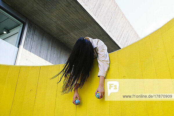 Unconscious young woman holding globes leaning on yellow wall