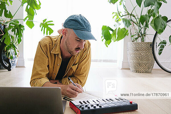 Man with piano and laptop writing in book at home
