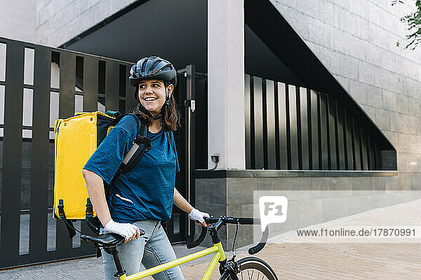 Lächelnder junger Zusteller mit Helm  der mit dem Fahrrad steht