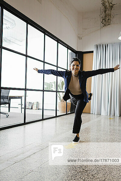 Carefree young businesswoman standing on one leg in office
