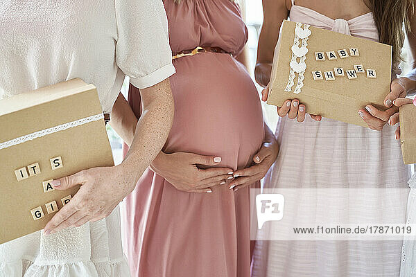 Pregnant woman standing with friends holding gift box