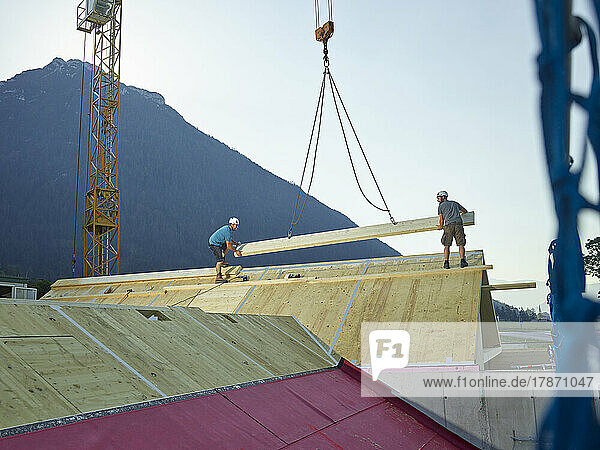 Carpenters installing rooftop with crane at construction site
